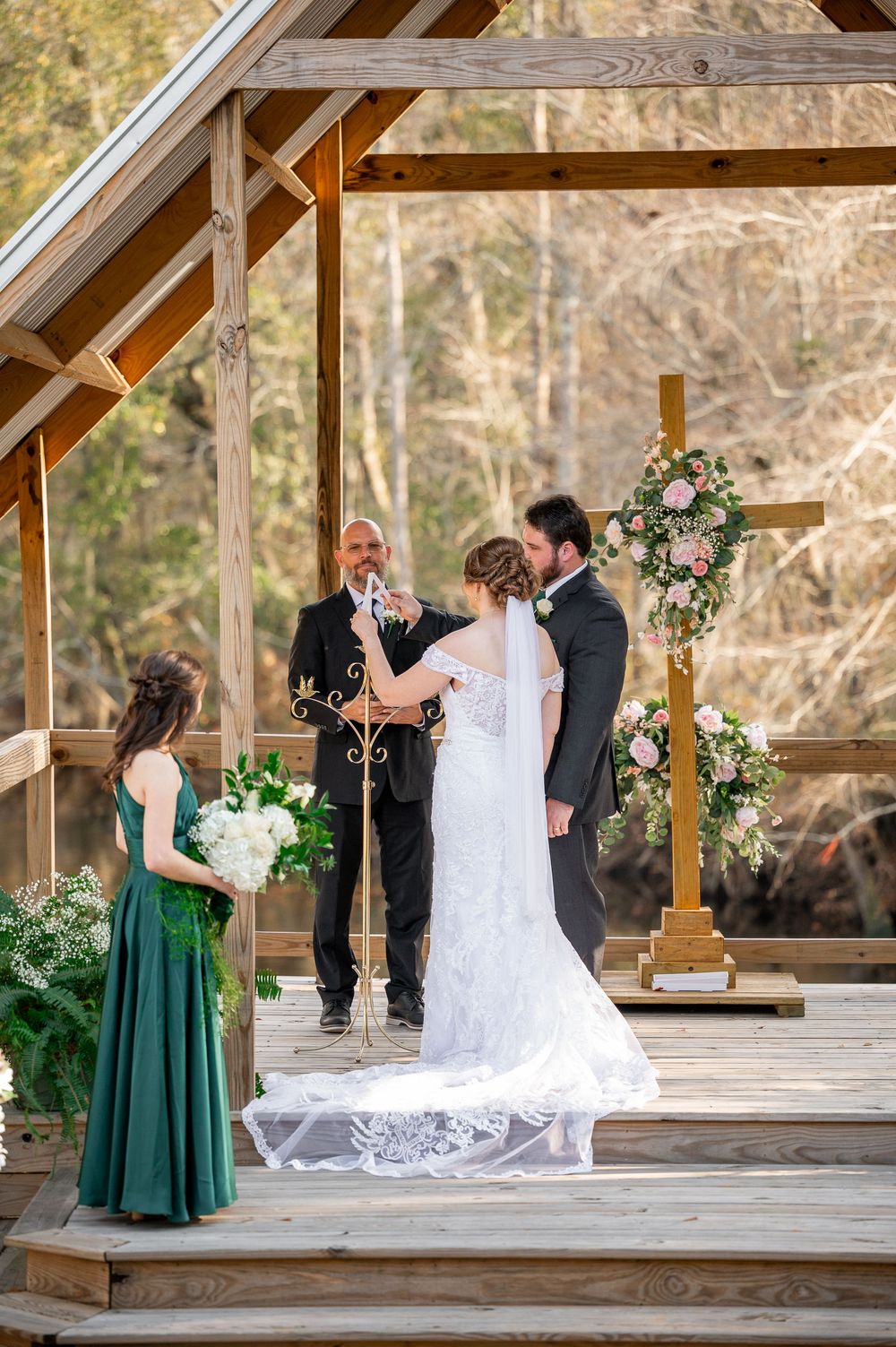 Wedding ceremony moments captured under wooden pavilion with emerald green bridesmaids dresses.