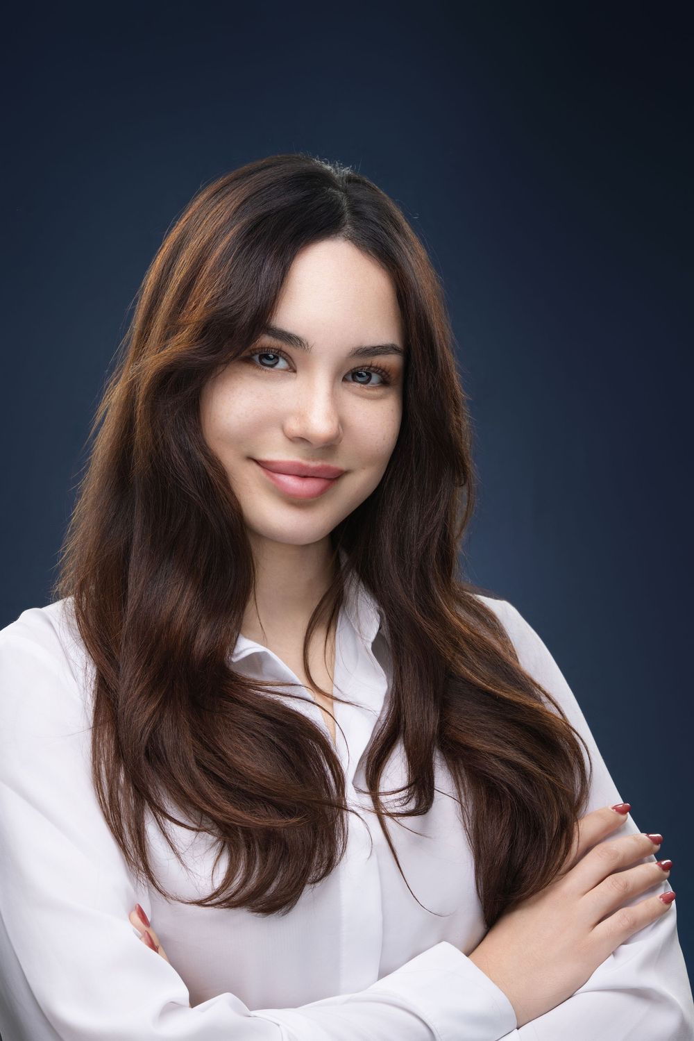 Professional studio portrait of a woman with long brown hair wearing a white button-down shirt against a dark background.