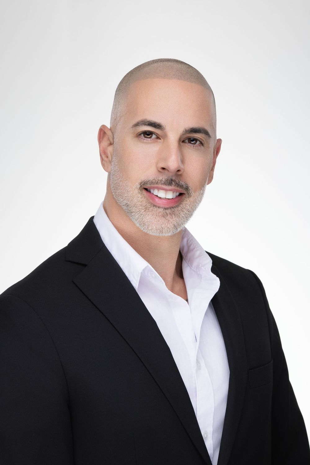 Professional headshot of a person in a black blazer and white dress shirt against a light gray background.
