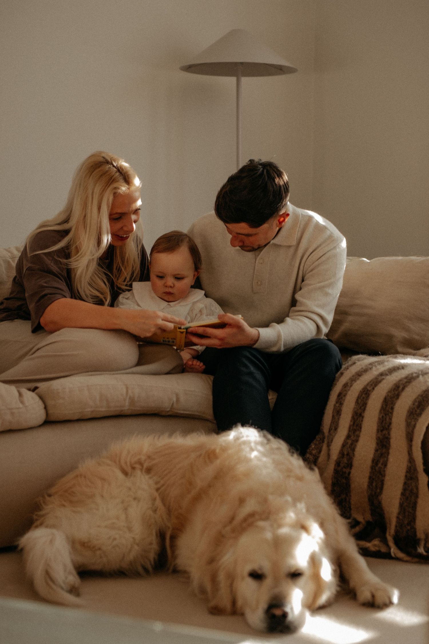 Relaxed family moment at home with parents and baby sitting together on the sofa while their dog rests nearby during a natural lifestyle fam