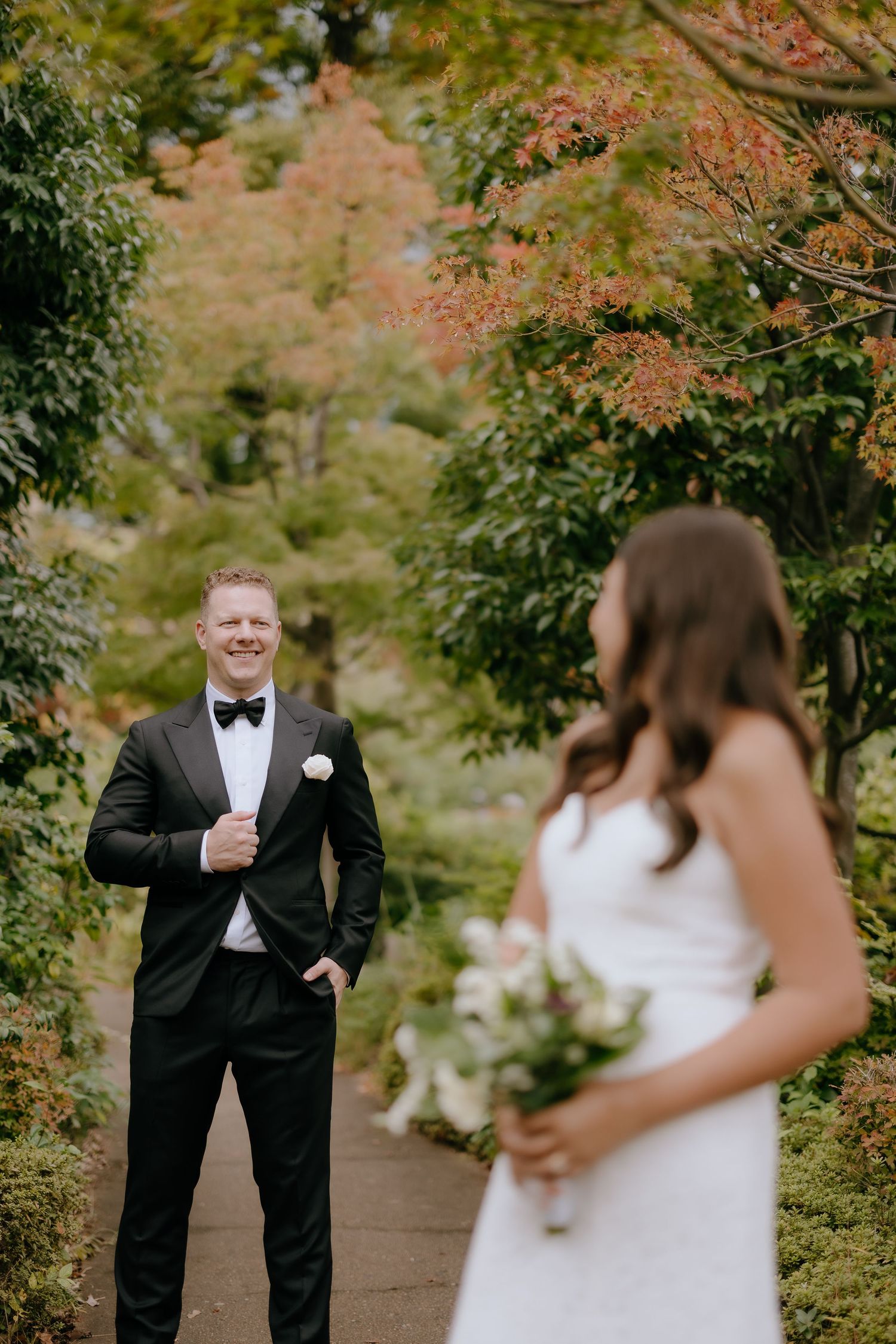 A wedding couple shares a joyful first look moment surrounded by autumn foliage in a garden setting.