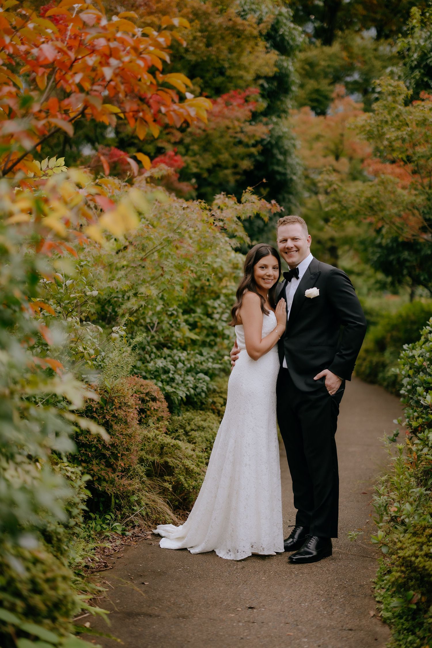 A couple shares a romantic moment on an autumn path surrounded by vibrant orange and red foliage.