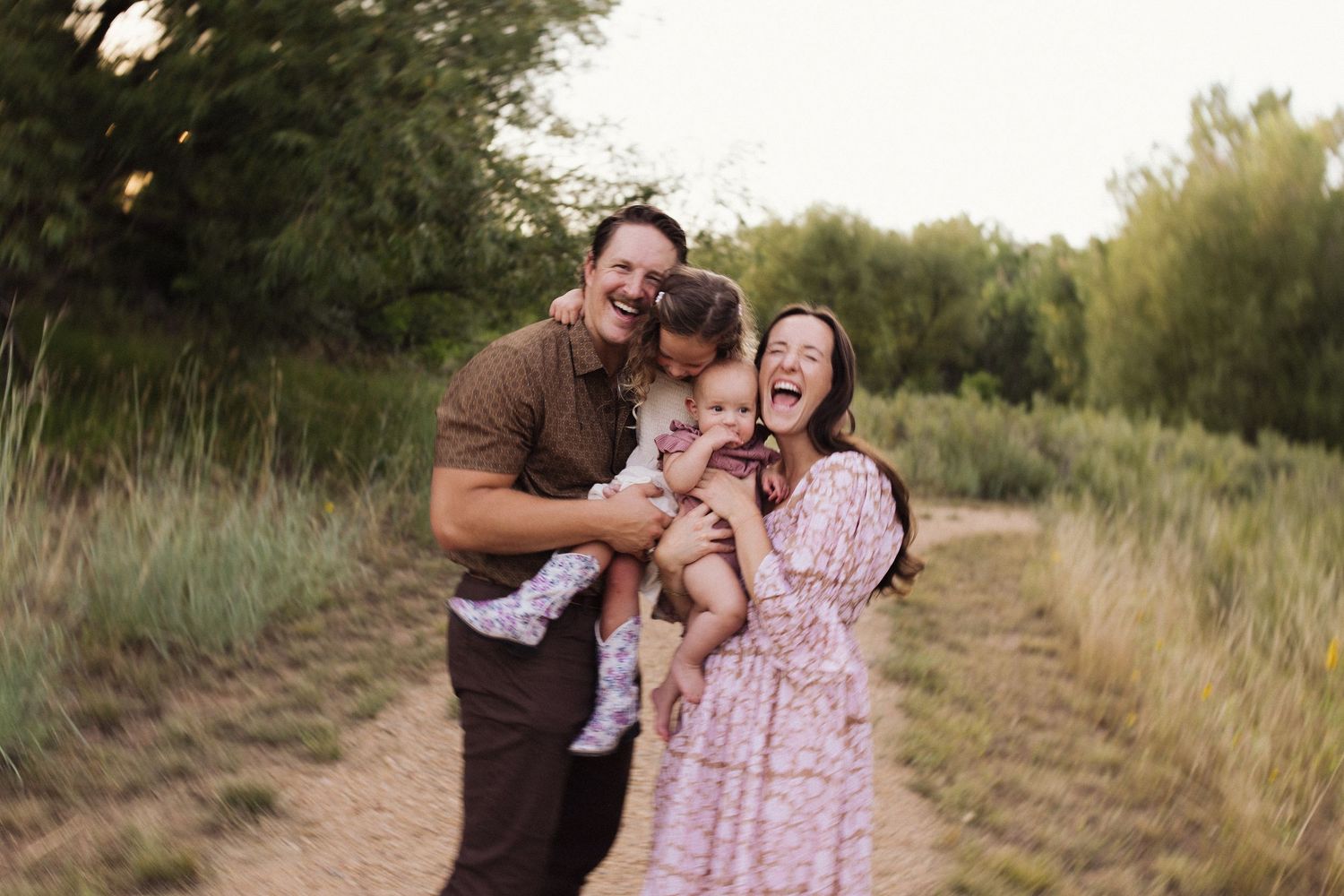 A couple embraces and laughs together during a sunset photoshoot in a grassy outdoor field.
