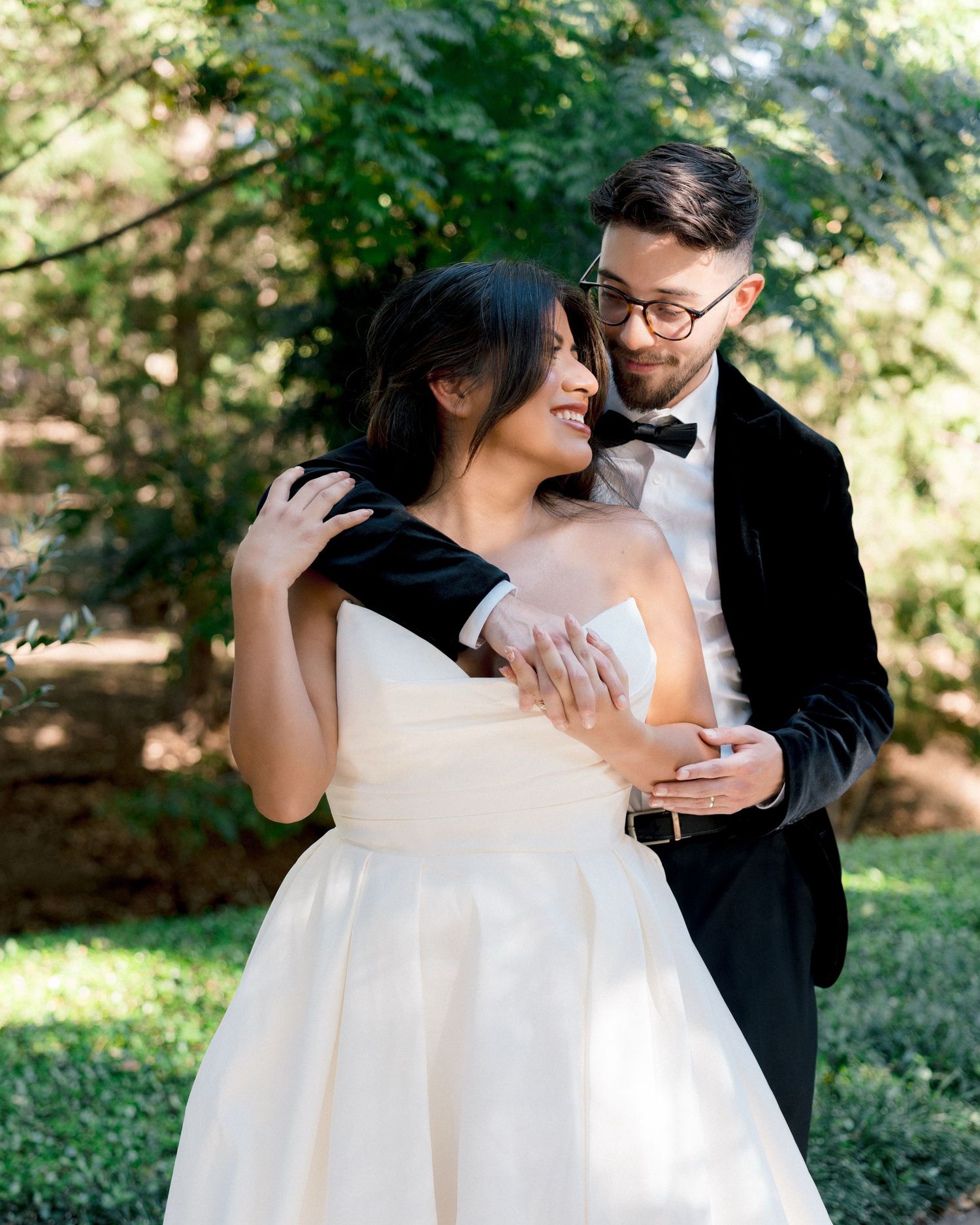 Bride and groom embracing during outdoor wedding portraits surrounded by natural greenery