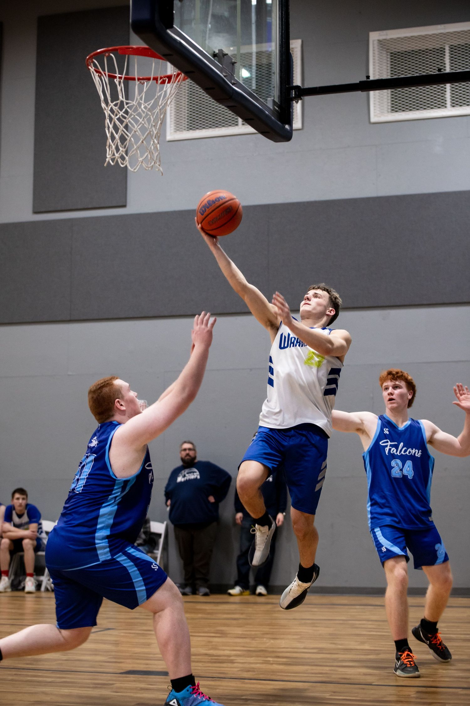 Two basketball players jump high to compete for a rebound during an intense indoor game.