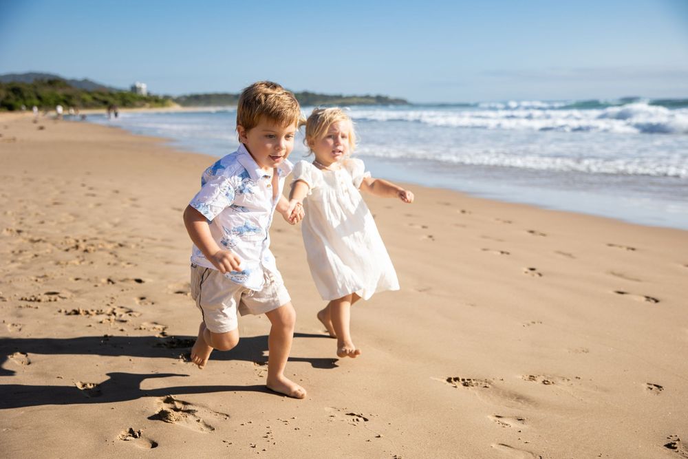 Children playing and running together on a sandy beach with ocean waves in the background.