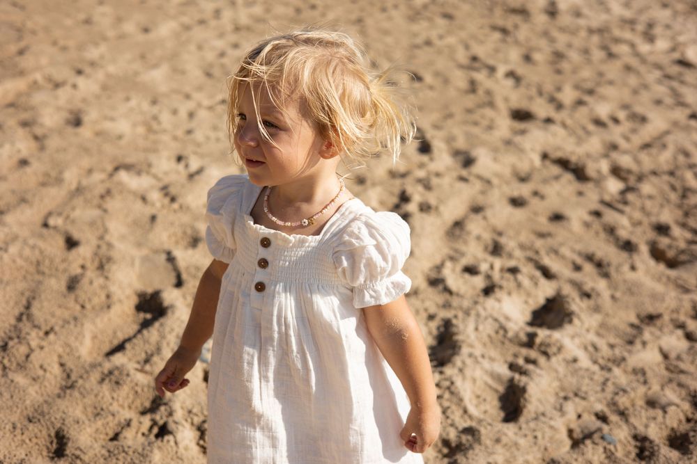 Child in white dress standing on sandy ground during golden hour sunlight.