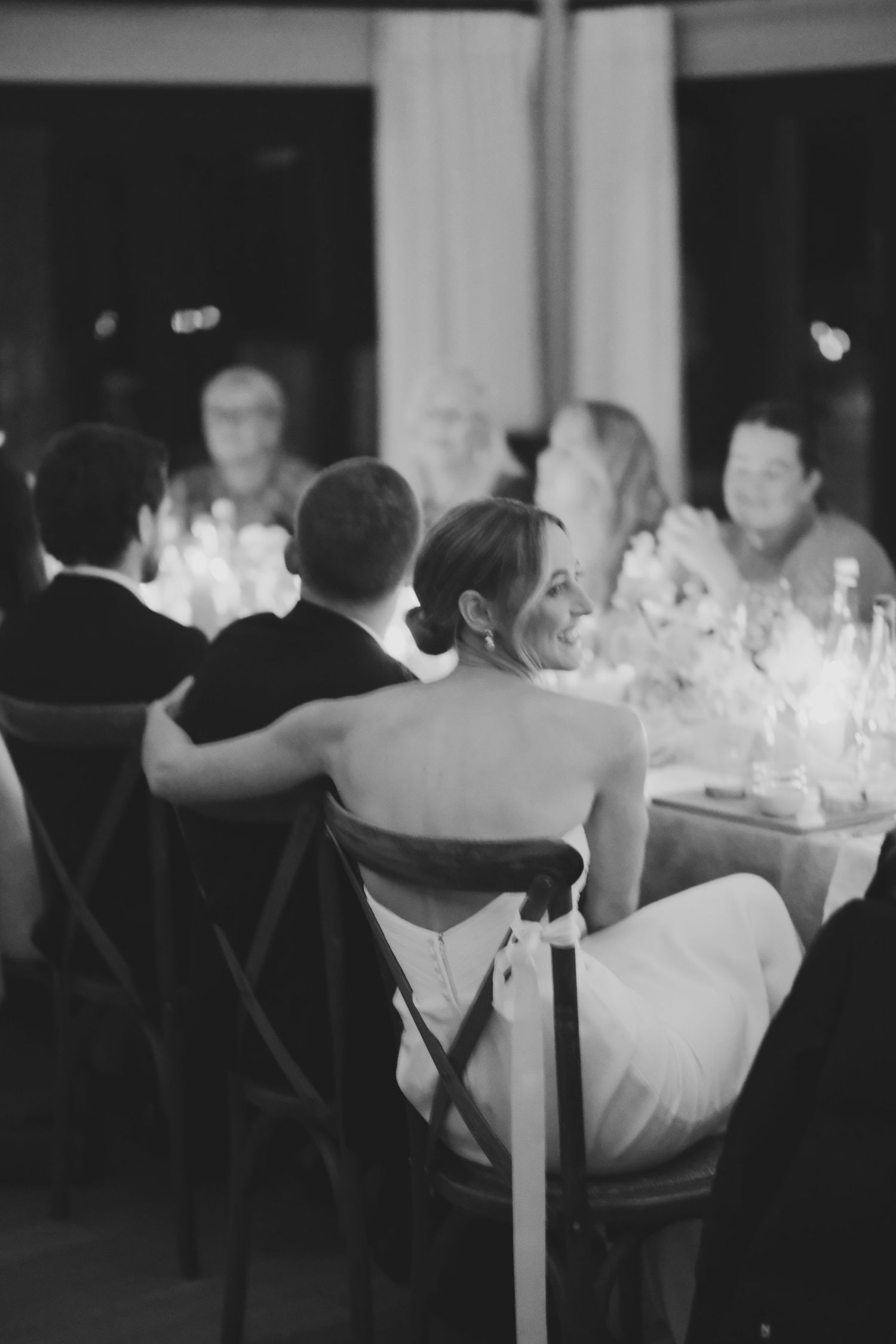 Black and white photo of a bride smiling at a candlelit wedding reception dinner table.