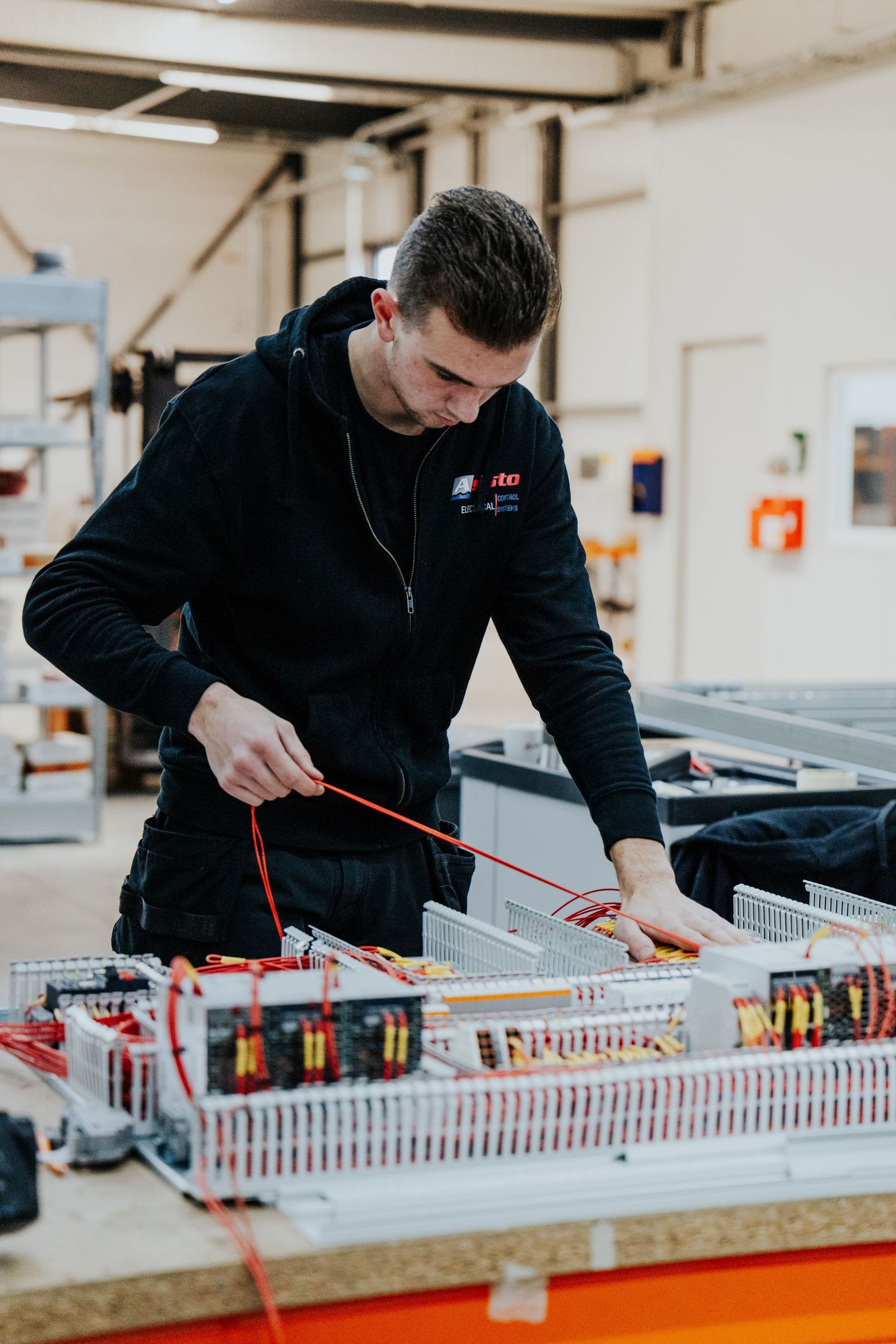 Technician working on electrical control panel wiring and assembly in industrial manufacturing facility.