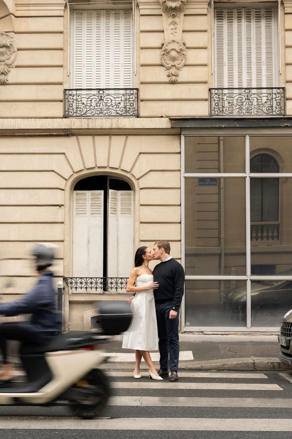 A romantic couple shares a tender moment on a Parisian street while blurred figures pass by in a cinematic sequence.
