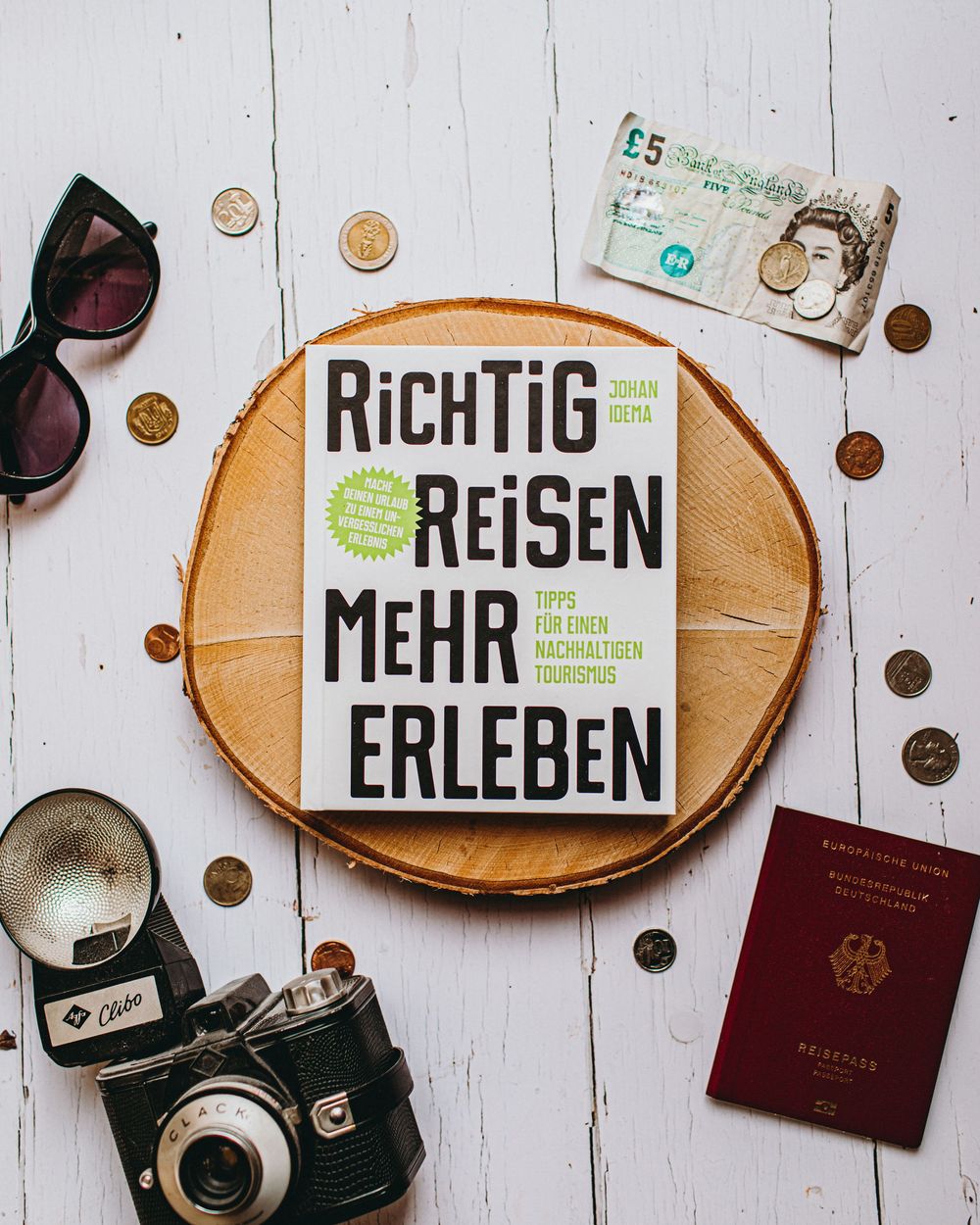 Travel items arranged on white wooden surface with passport, sunglasses, coins, and wooden signs with German text.