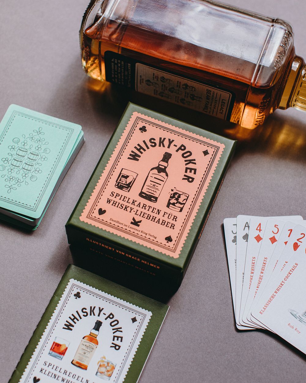 Whiskey Poker playing cards and branded boxes displayed on a gray surface with warm lighting and vintage aesthetic.