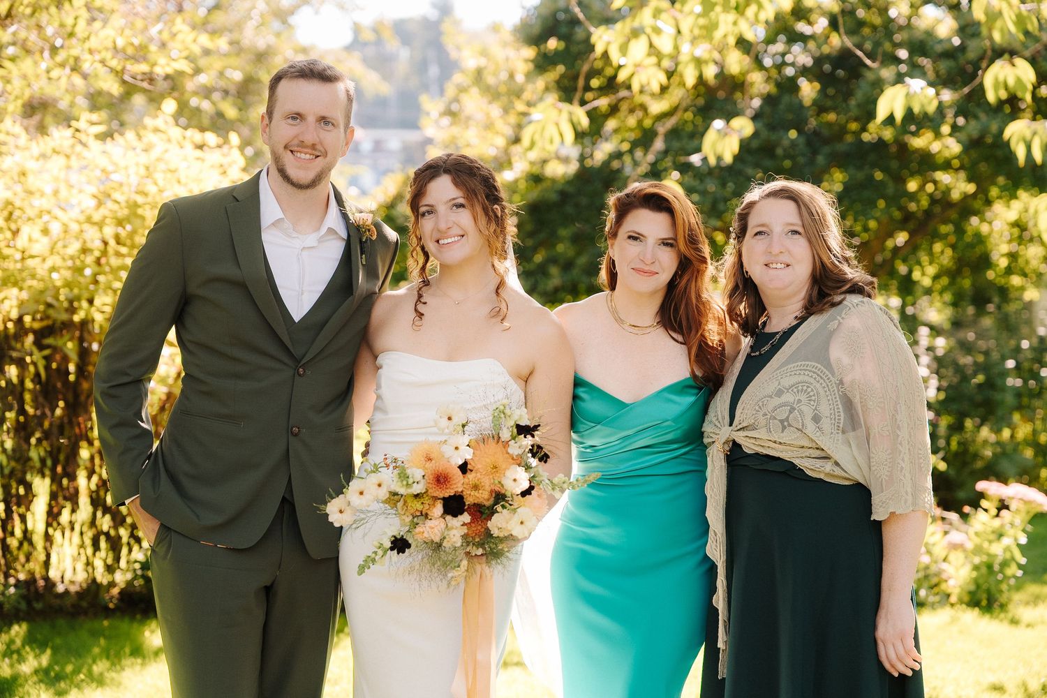 Wedding party poses outdoors in formal attire with turquoise bridesmaids dresses and sunflowers in golden sunlight.
