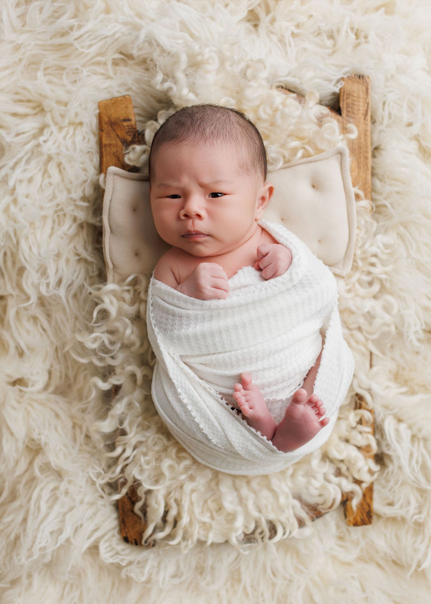 A sleeping newborn swaddled in white fabric lies on a cream-colored textured blanket in a series of peaceful poses.