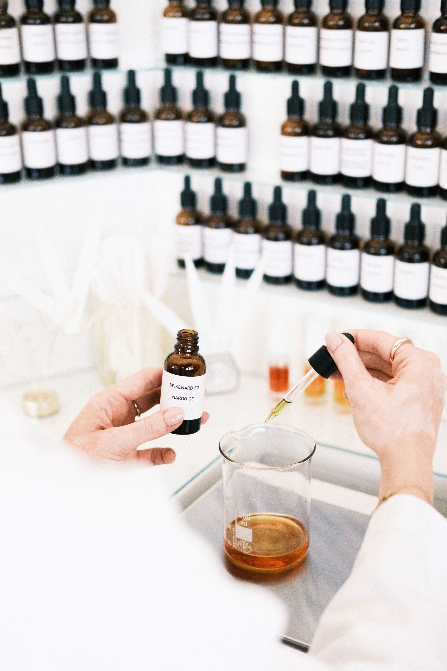 Rows of small amber glass dropper bottles arranged in a line with white labels and caps on a light surface.