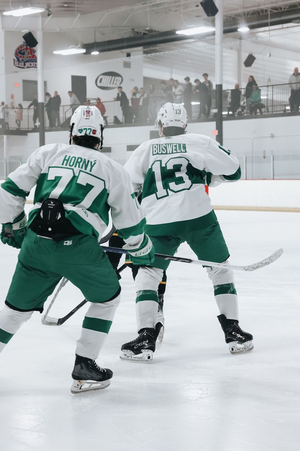 Hockey players in green and white jerseys skate in formation during practice.