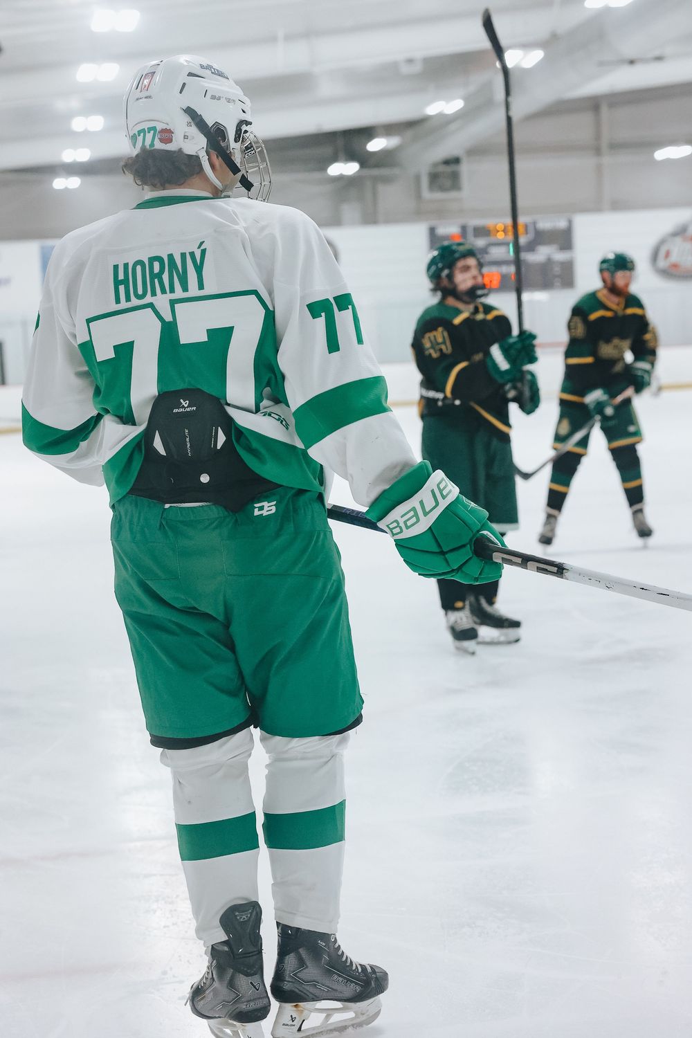 Hockey players in green and white uniforms skating on ice during a game.