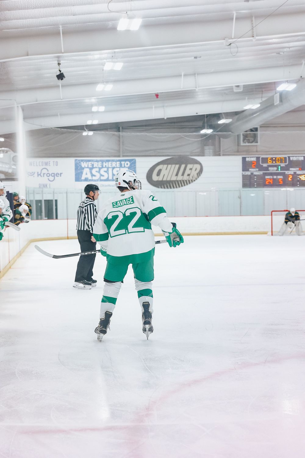 Hockey player in green and white jersey number 22 skating on ice rink with referee in background.