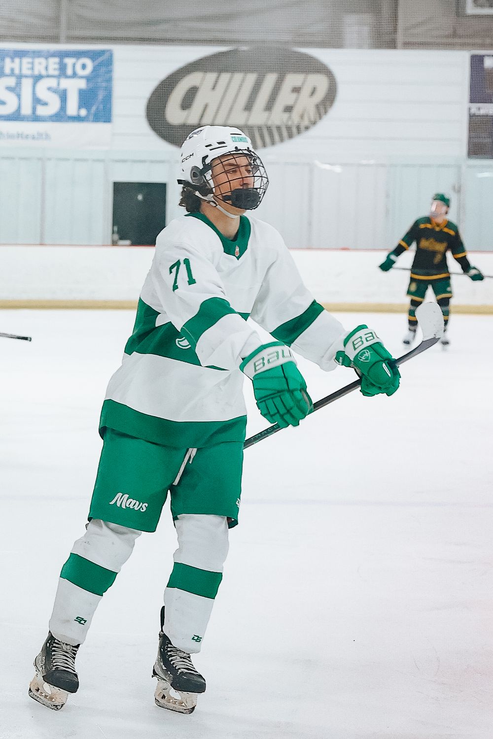 Hockey player in white and green uniform with number 71 skating during game.
