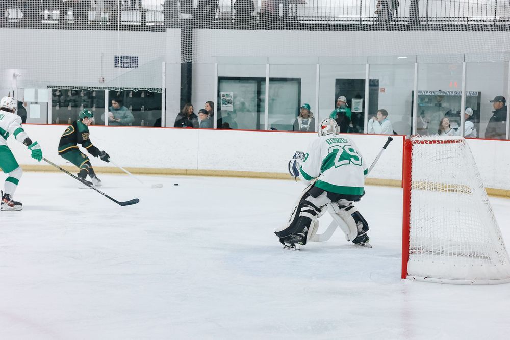 Hockey action shot showing goalie defending net during intense game play.