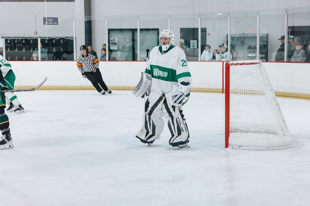 Hockey goalie in white and green uniform positioned near goal post during game.