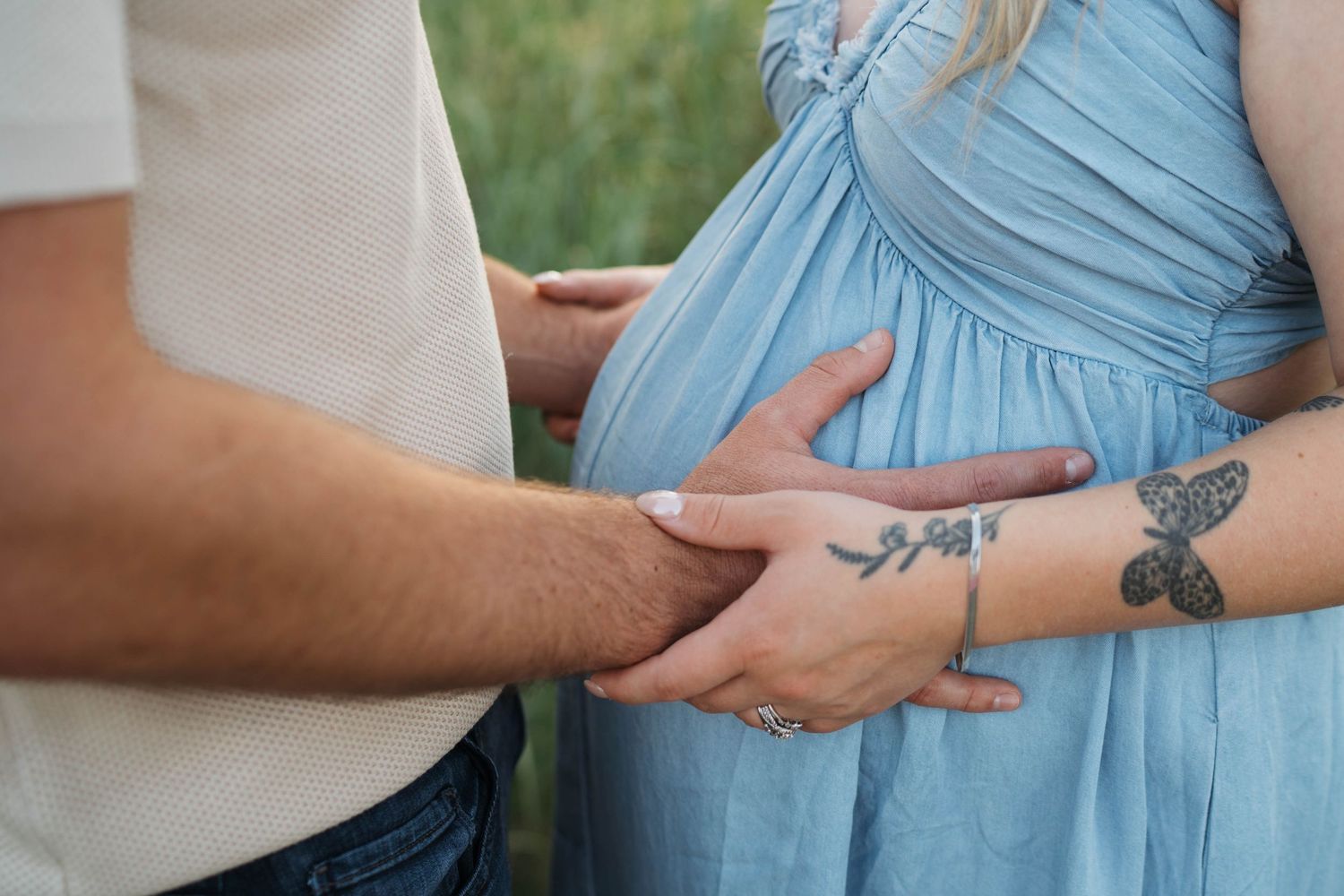 Expecting couple in white shirt and jeans embrace during intimate maternity photo session in bright studio setting.