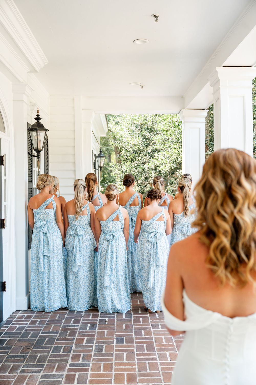 Wedding party in light blue dresses lined up on brick porch with white columns.