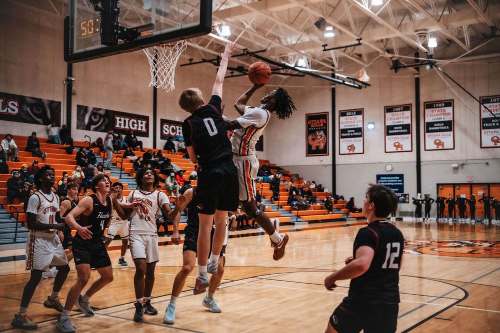 Basketball player makes dramatic jump shot during intense game in high school gymnasium.