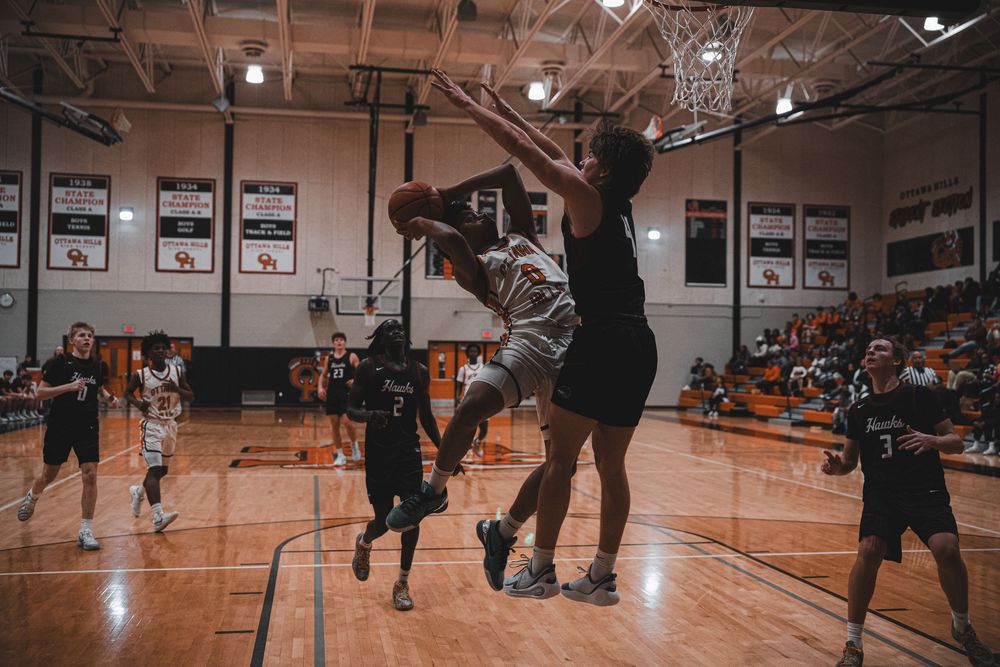 Basketball players compete for the ball during intense game action in school gymnasium.