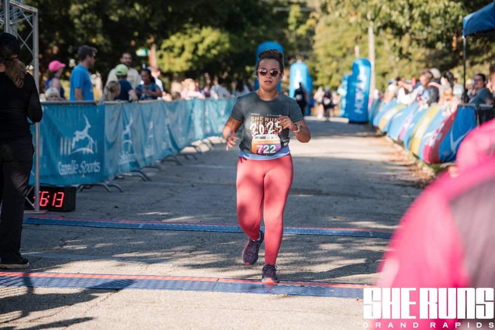 Athletes approach finish line on tree-lined course during running competition.