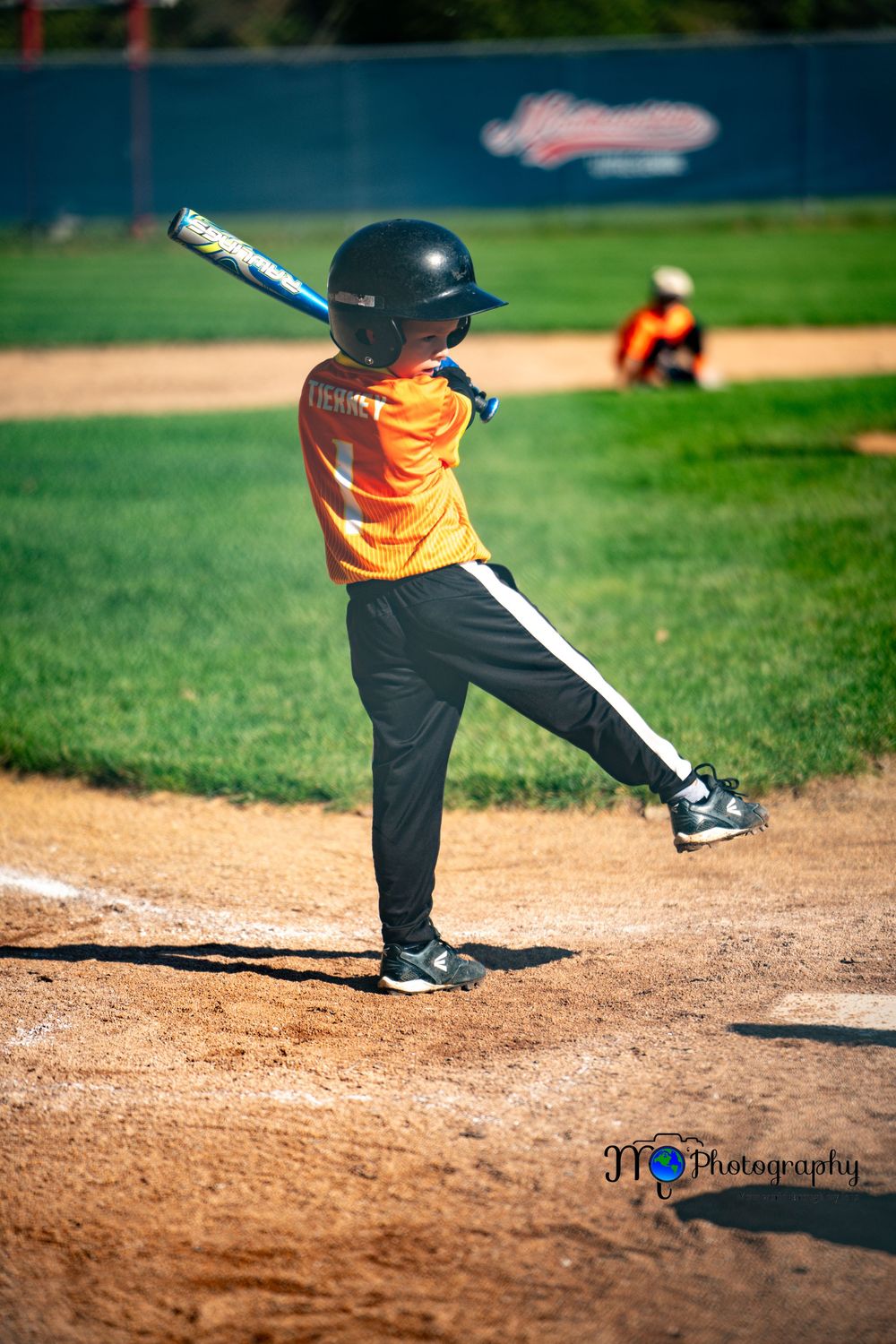 Young baseball player in orange uniform follows through on batting swing.