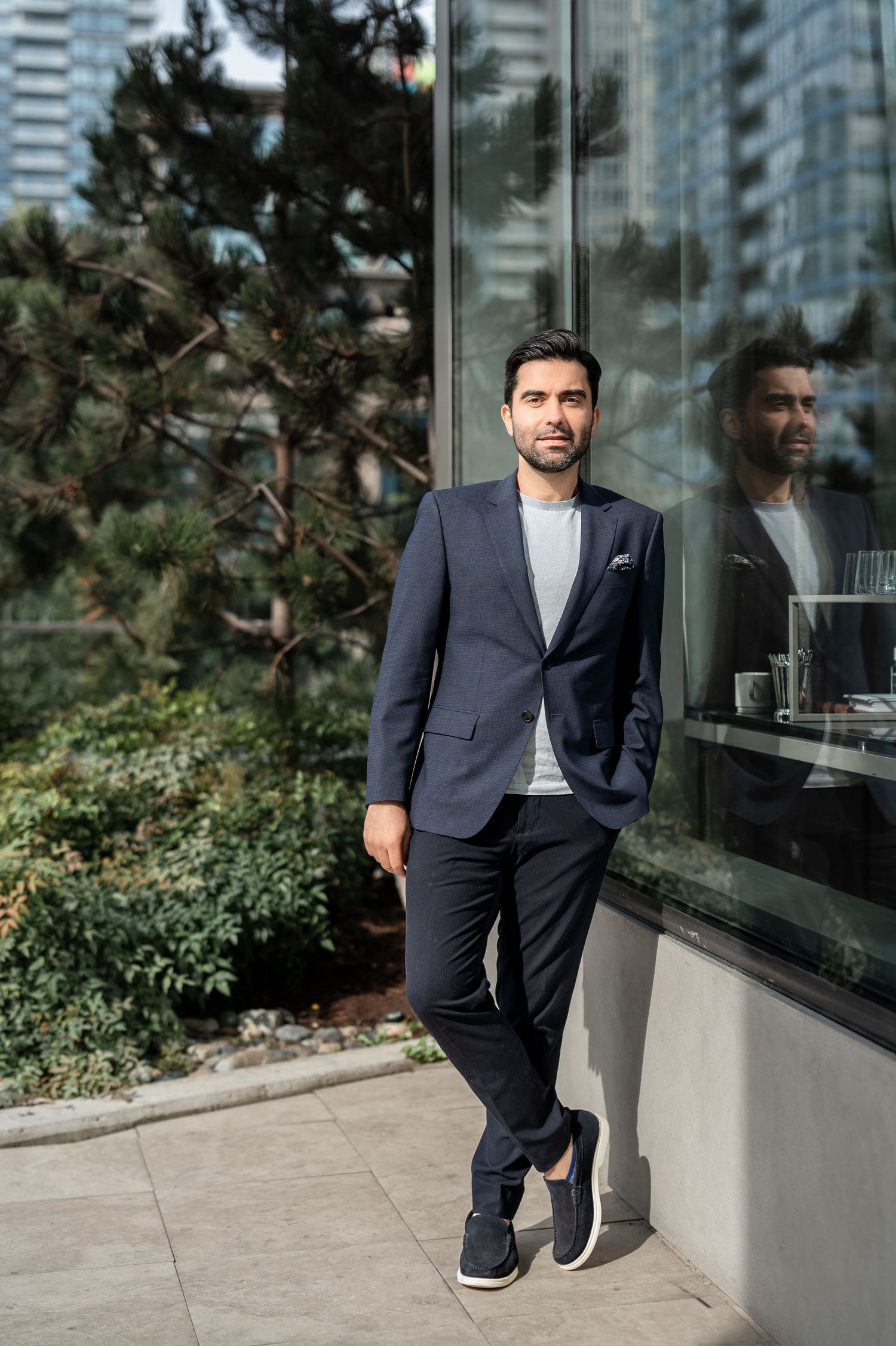 Professional in a navy suit and sneakers poses against modern glass building exterior with urban landscaping.