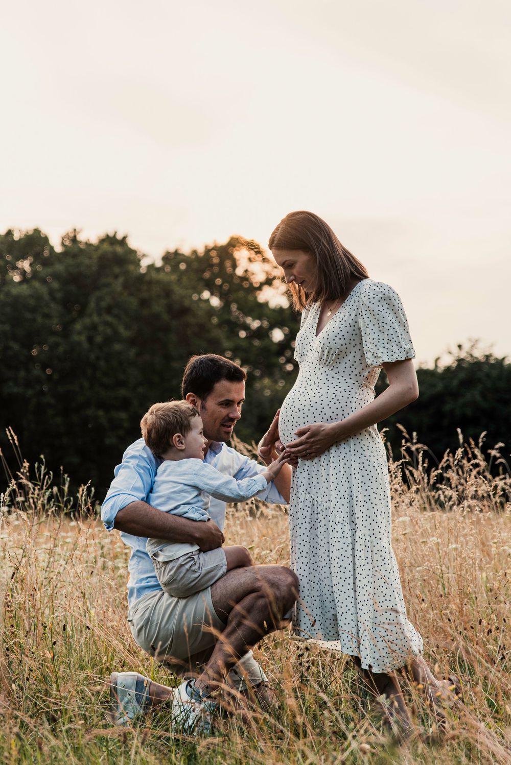 A family shares a tender moment in a golden field at sunset as they await their new arrival.