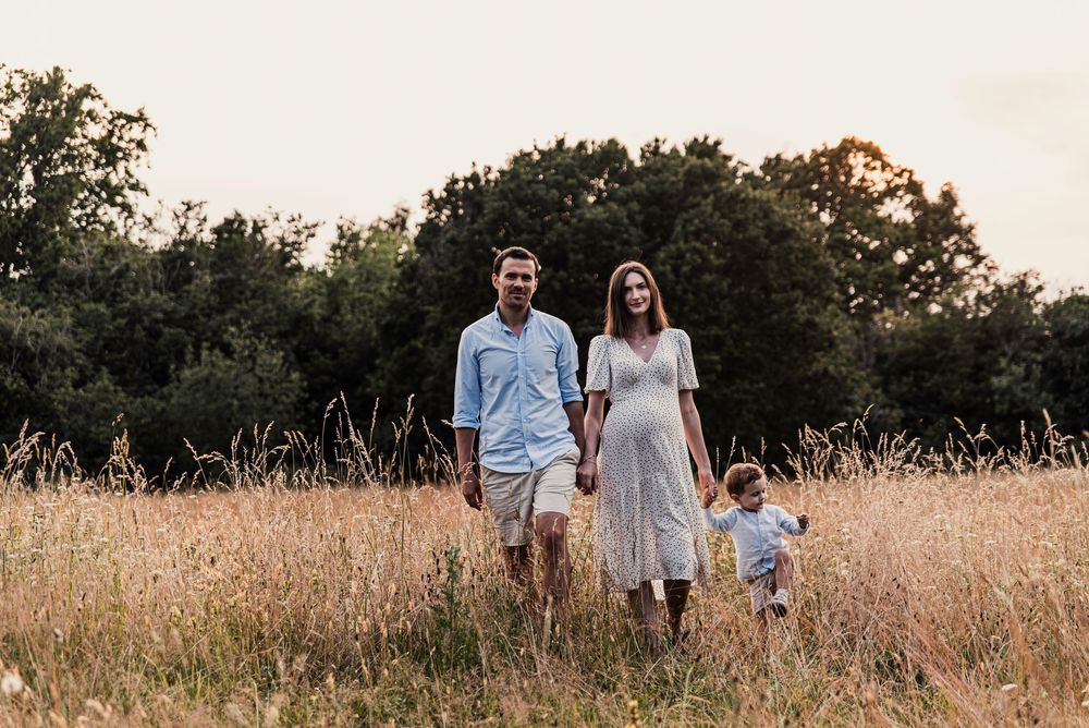 Family walking together through a golden wheat field at sunset in matching light blue and white outfits.