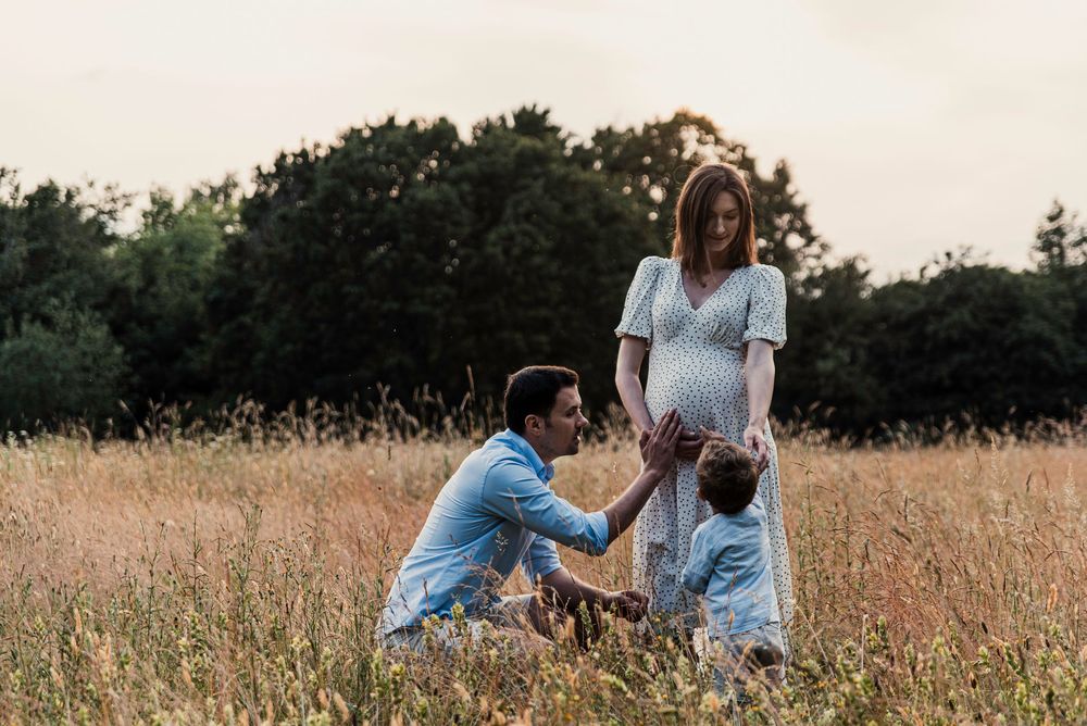 A family in a golden field during sunset shares a tender moment touching the mother's pregnant belly.