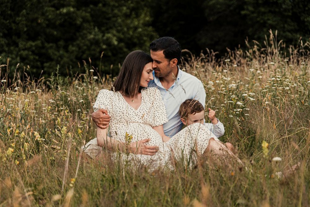 A couple shares an intimate moment while sitting together in a wildflower meadow on a sunny evening with their young son.