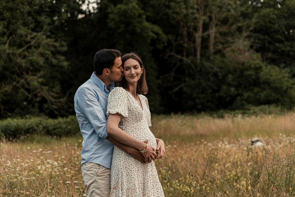 A couple embraces in a golden meadow during sunset with trees in the background.