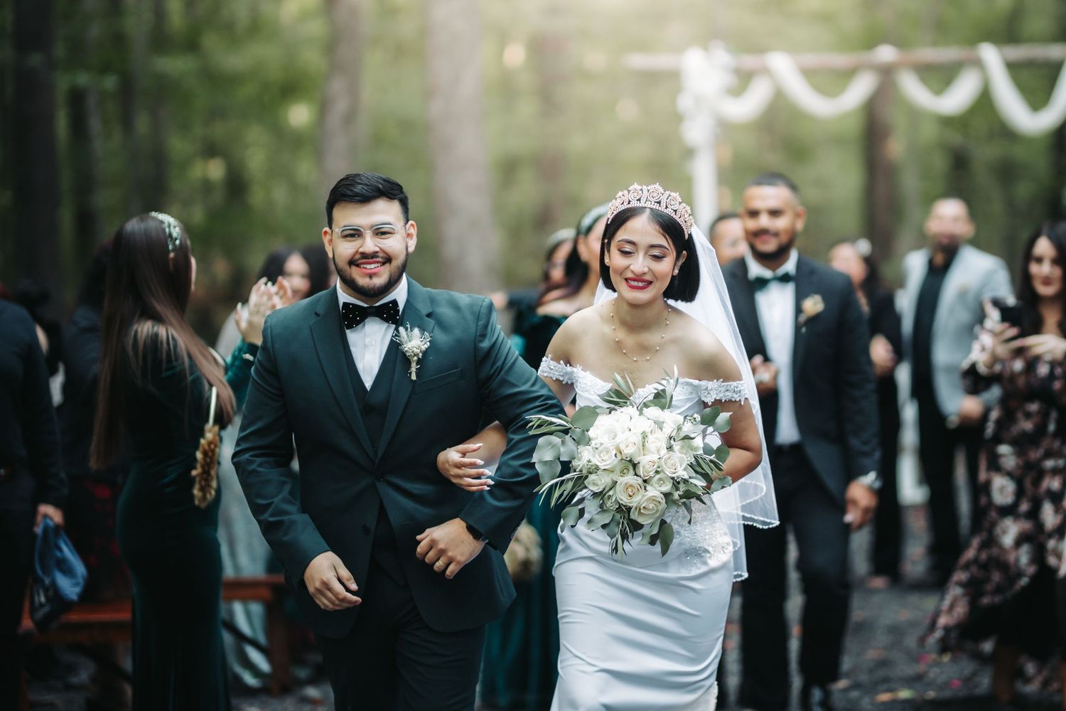 A joyful couple walks down the aisle together at an outdoor wedding ceremony while guests look on.