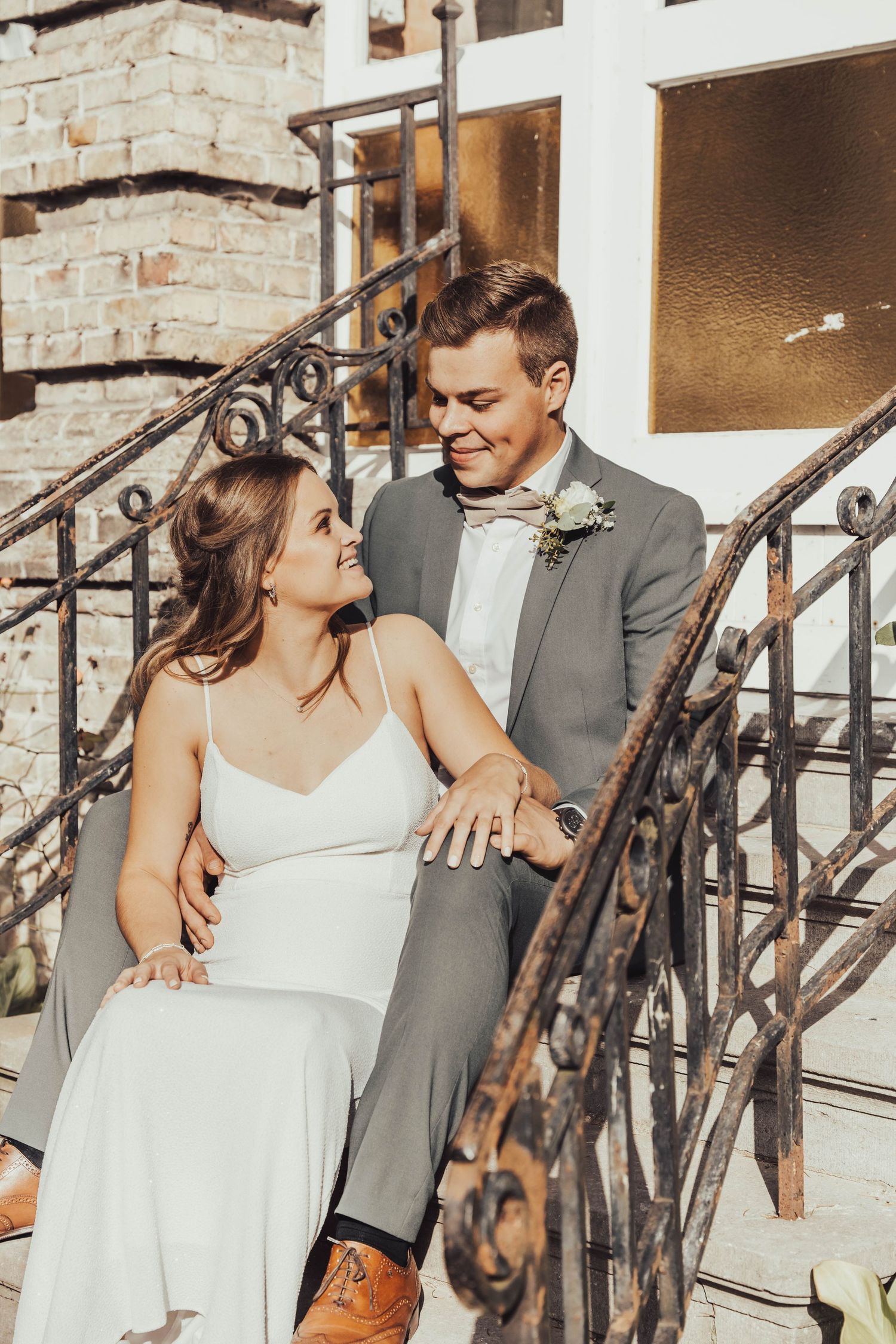 A couple shares a sweet moment on vintage iron stairs against brick architecture.