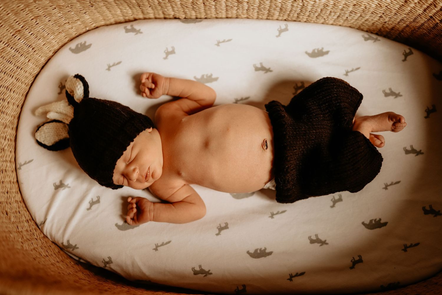 Sleeping newborn wearing black outfit lying on white patterned bedding.
