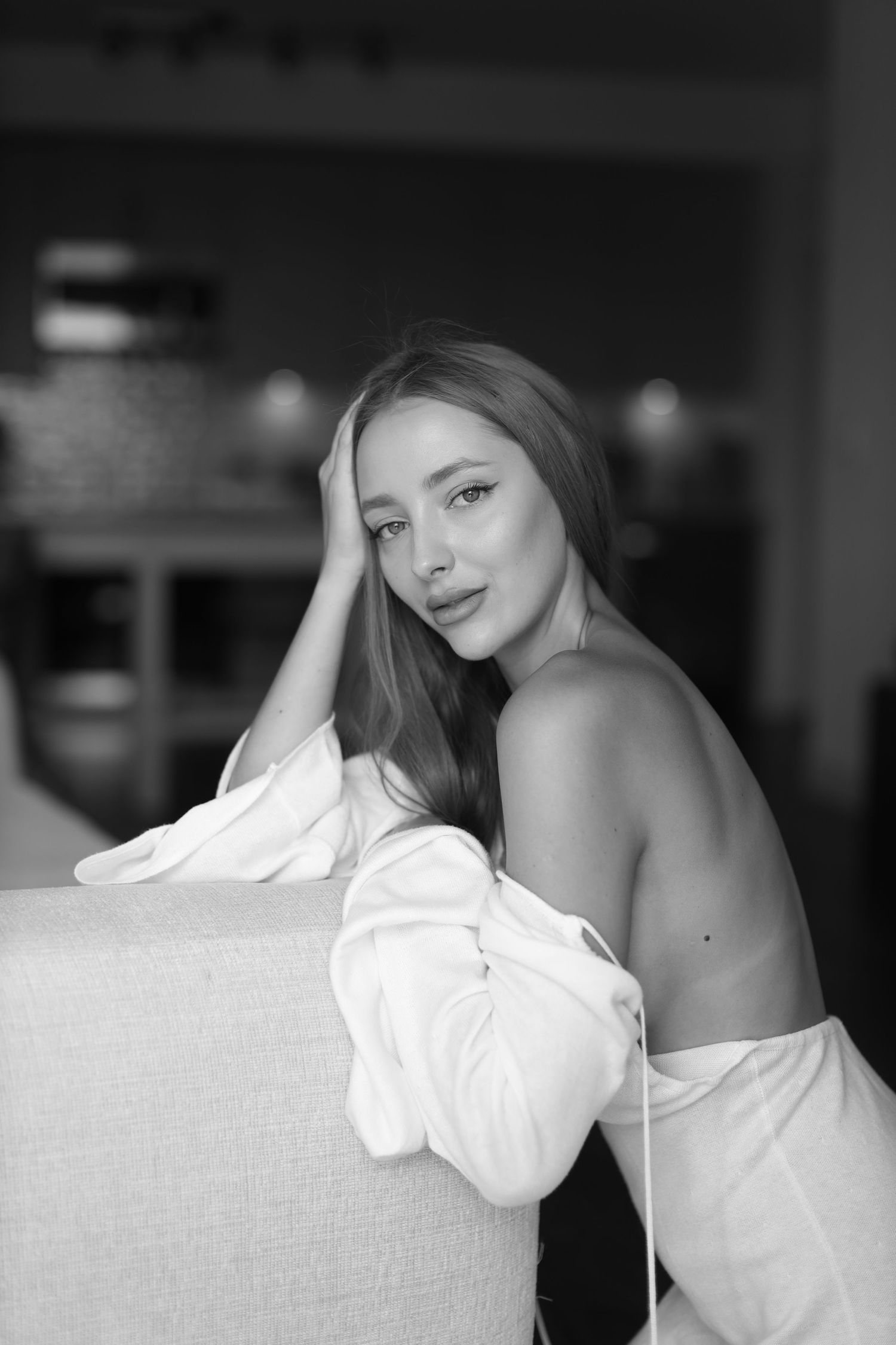 Black and white boudoir photo of a woman posing on a couch in a white shirt.
