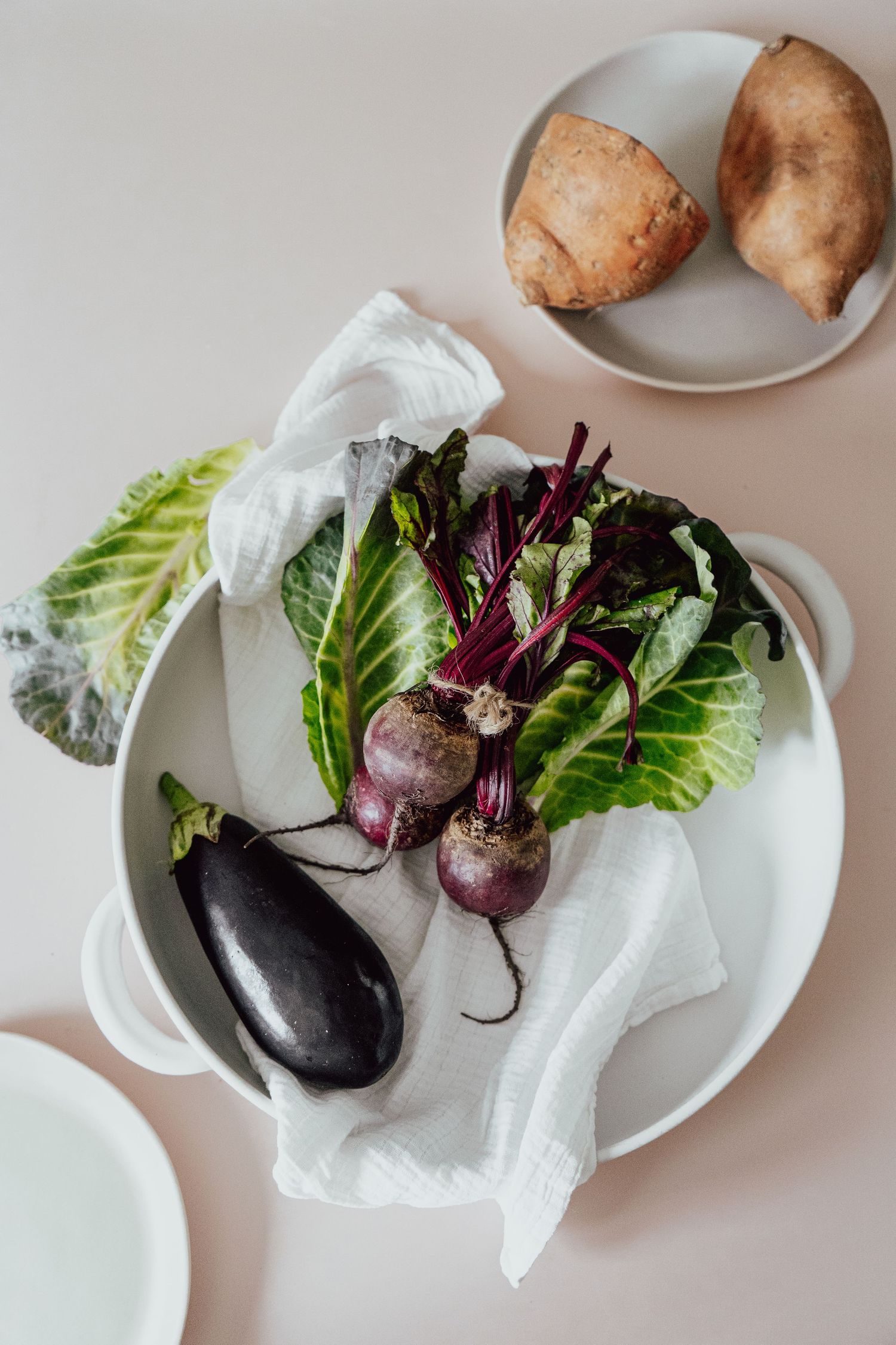 a flat lay photo of an aubergine, sweet potato and beetroot in cooking ware