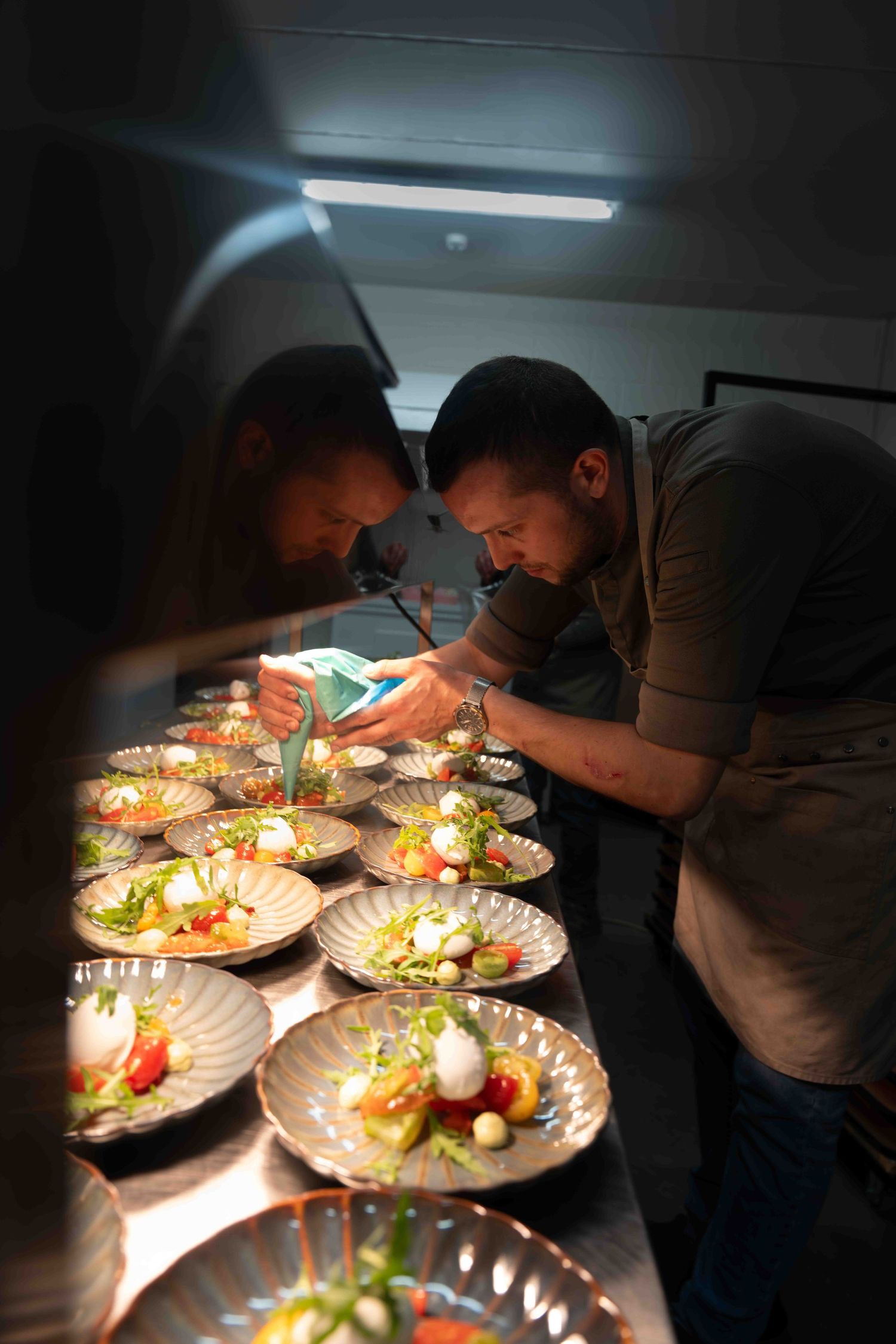 Chefs carefully plating dishes under focused lighting in a professional kitchen.