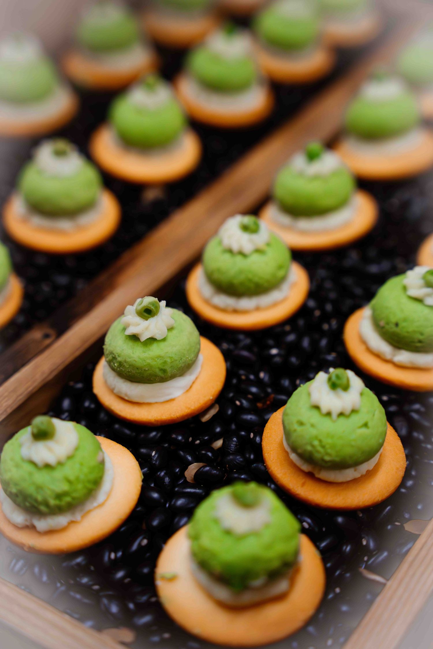 Precisely arranged green macarons with white garnish on orange bases.
