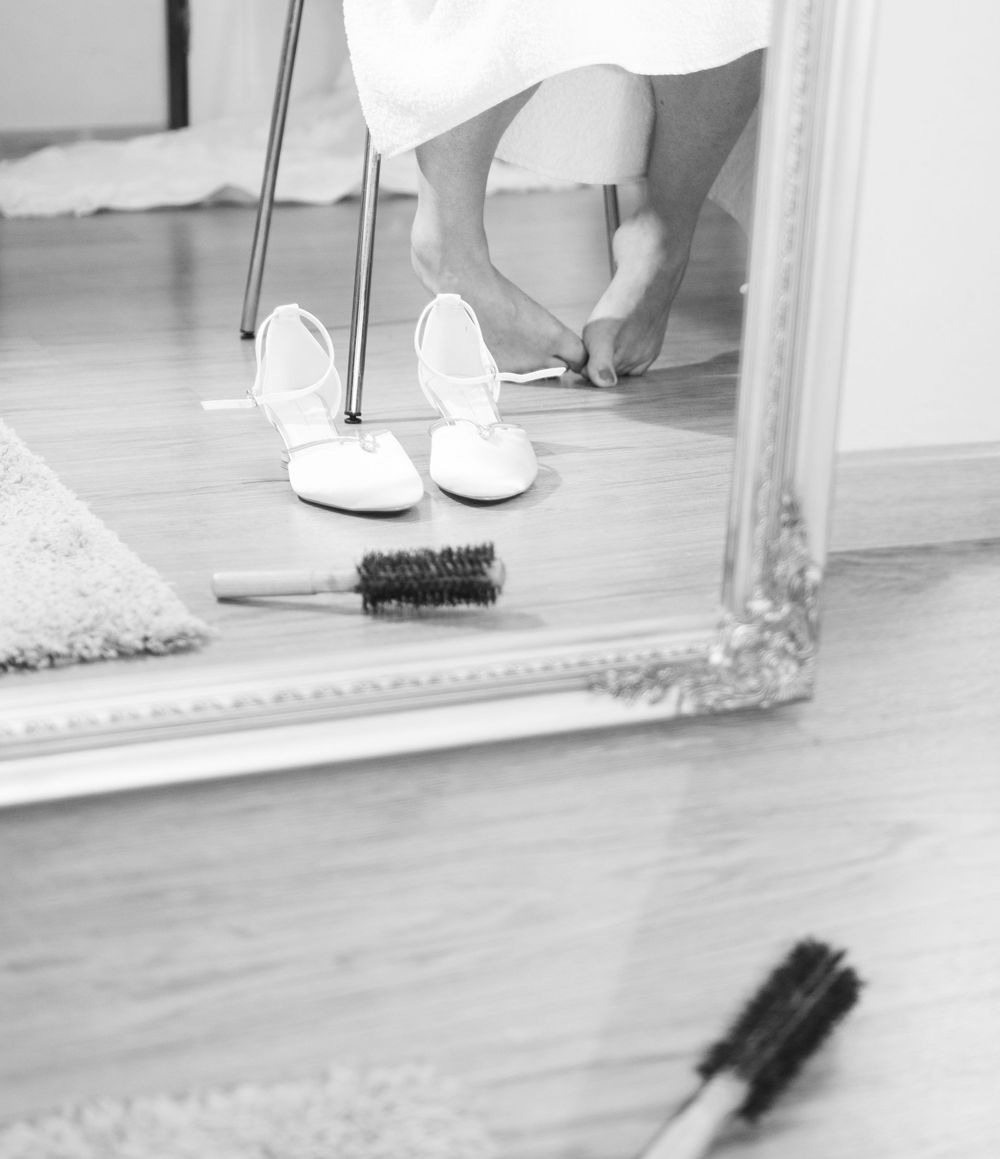 Black and white detail shot of bridal shoes reflected in an ornate floor mirror.