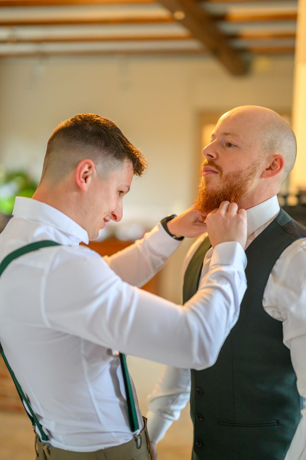 Groomsmen in white shirts and dark vests helping each other get ready.