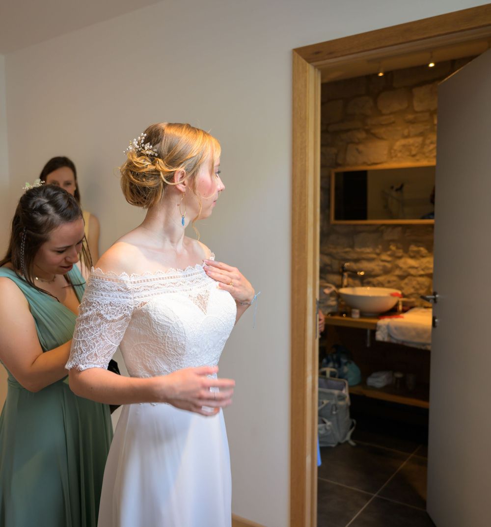 Bridesmaids helping to button up the back of a lace wedding dress.