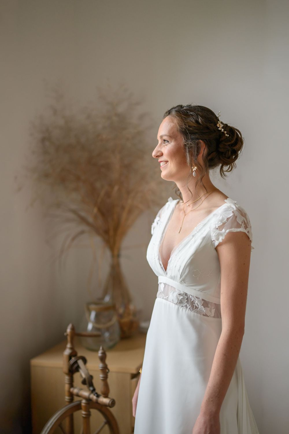 Elegant white wedding dress with lace cap sleeves and empire waist shown in soft natural lighting with dried flowers.