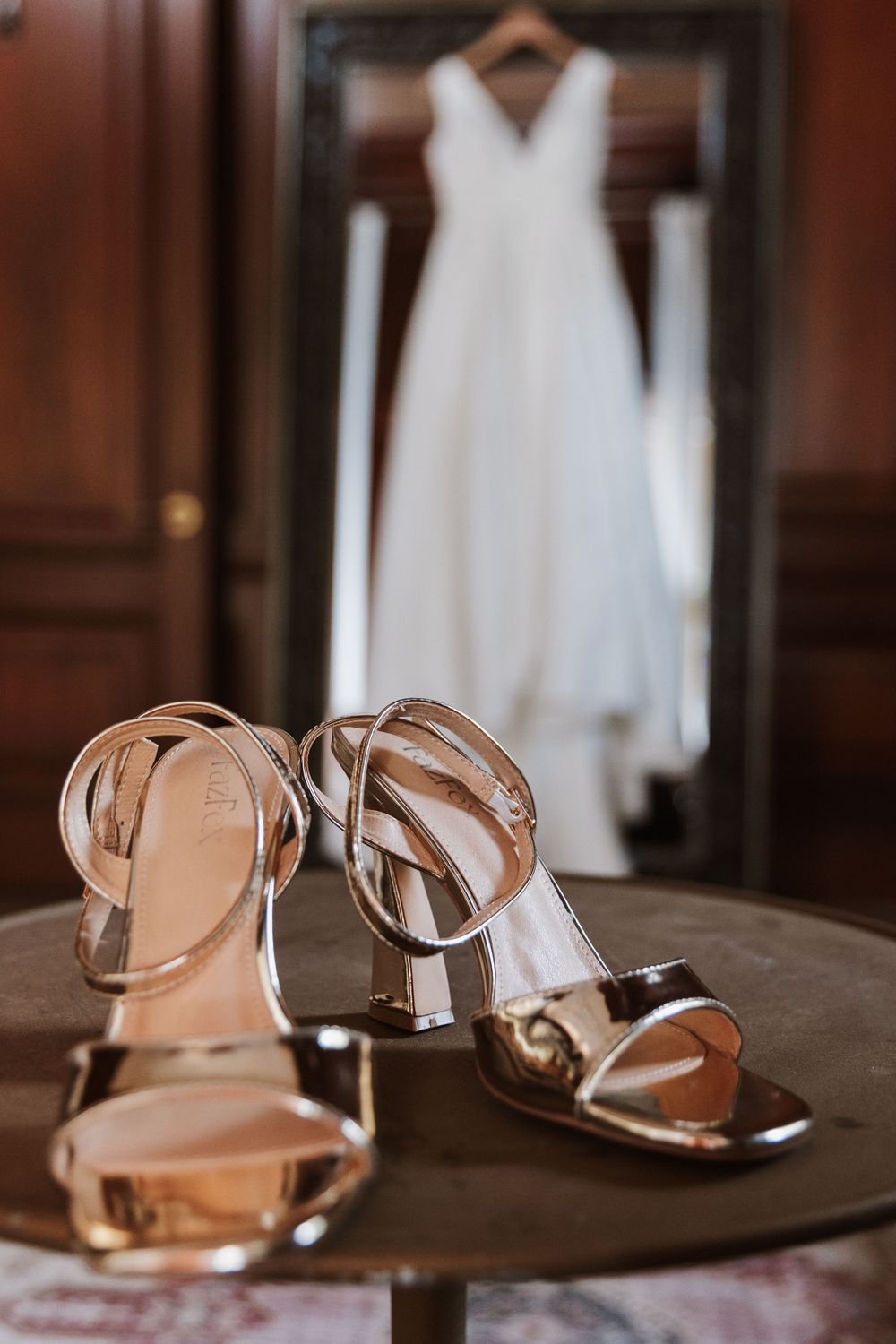 Metallic silver wedding sandals with reflection of white dress in background.