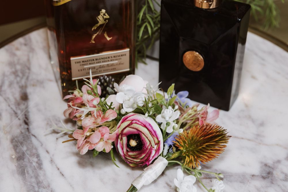Wedding detail shot of floral arrangement with Johnnie Walker whiskey bottle.
